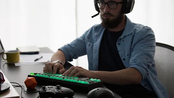 A man wearing a gaming headset sits at a desk with a gaming keyboard, Xbox手柄, 和一个地下城 & 龙死.